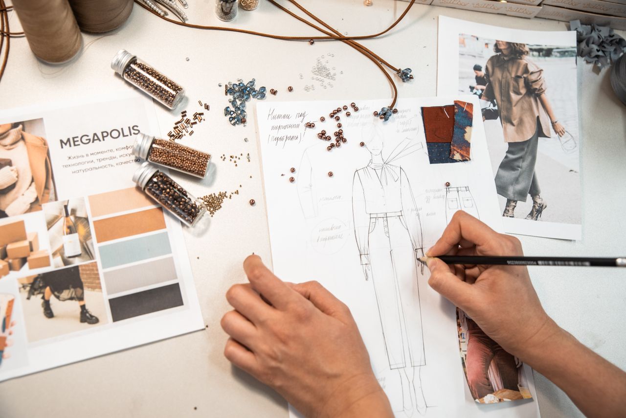 Features Fashion designer sketching in a workspace with materials and mood boards.