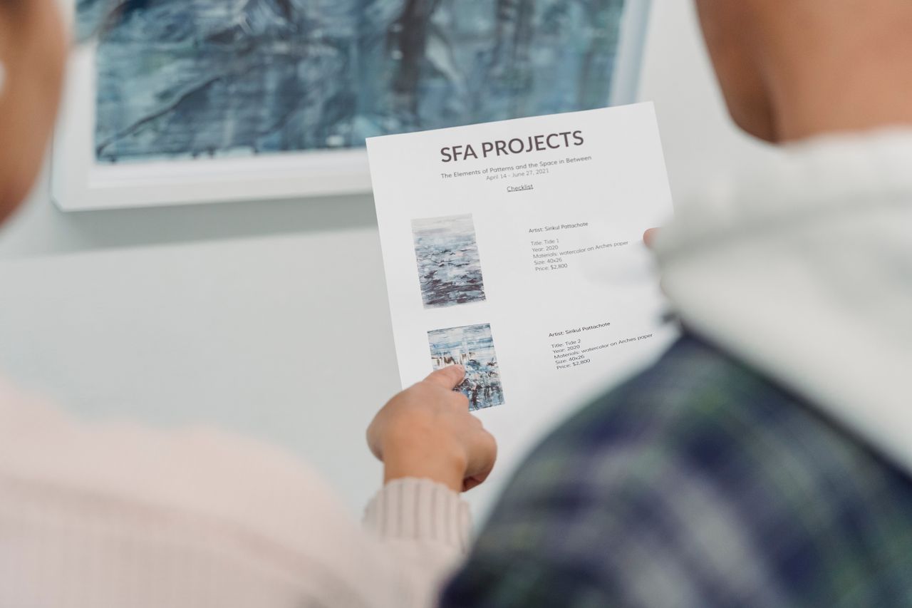 Features Close-up of hands holding and pointing at a project document during a meeting, featuring artistic project details.