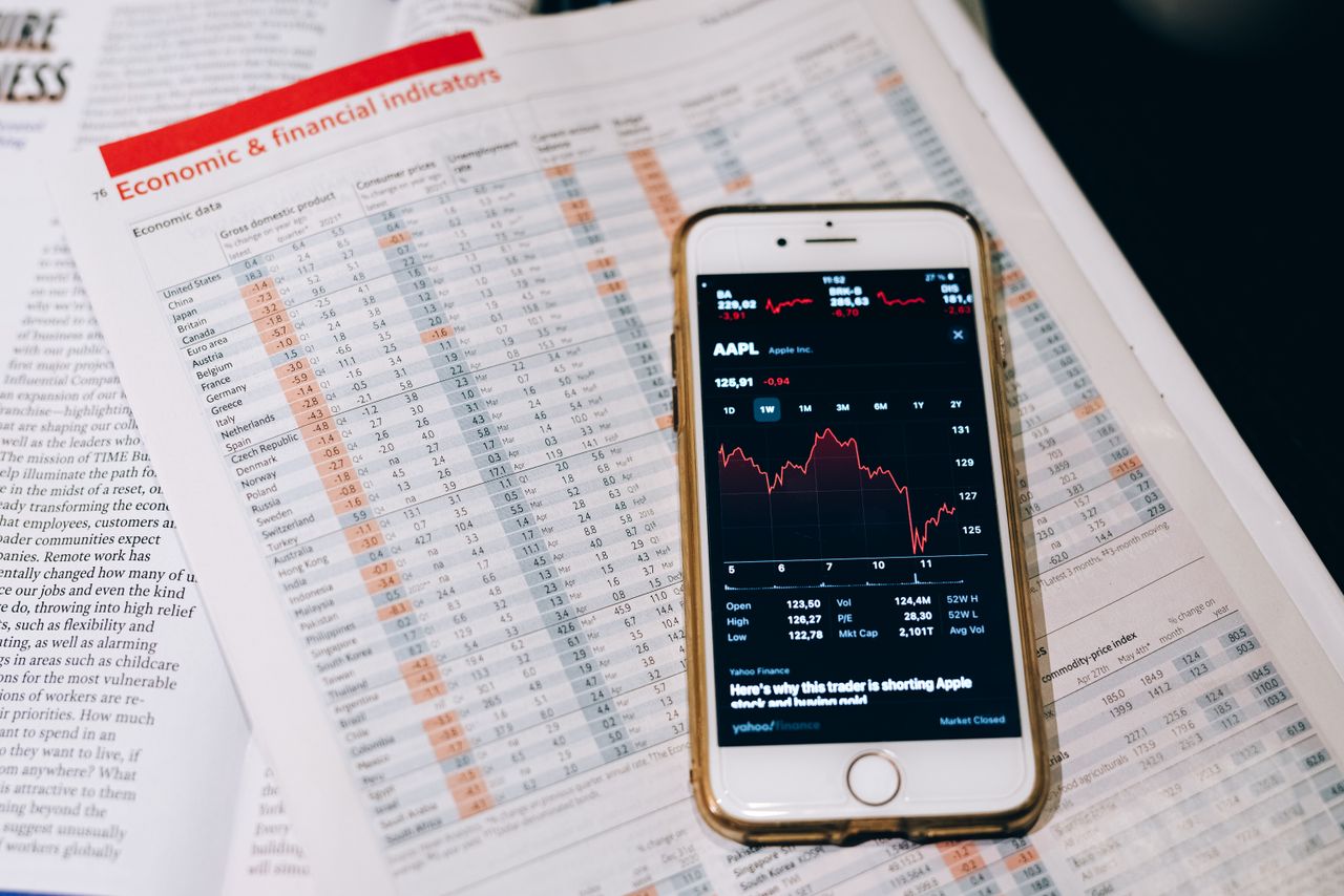 Features Smartphone displaying stock market data on papers with financial charts.