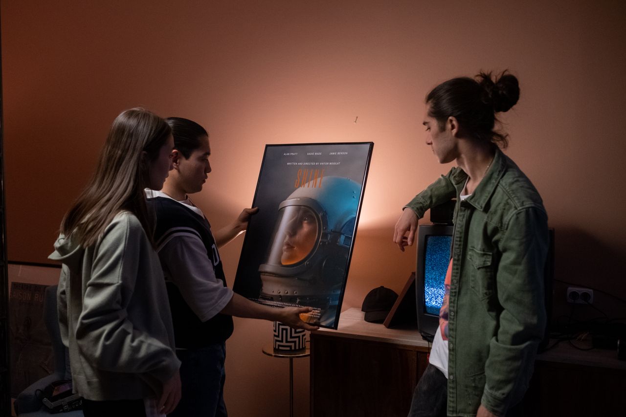 About Group of teenagers discussing a poster indoors in a cozy home setting.